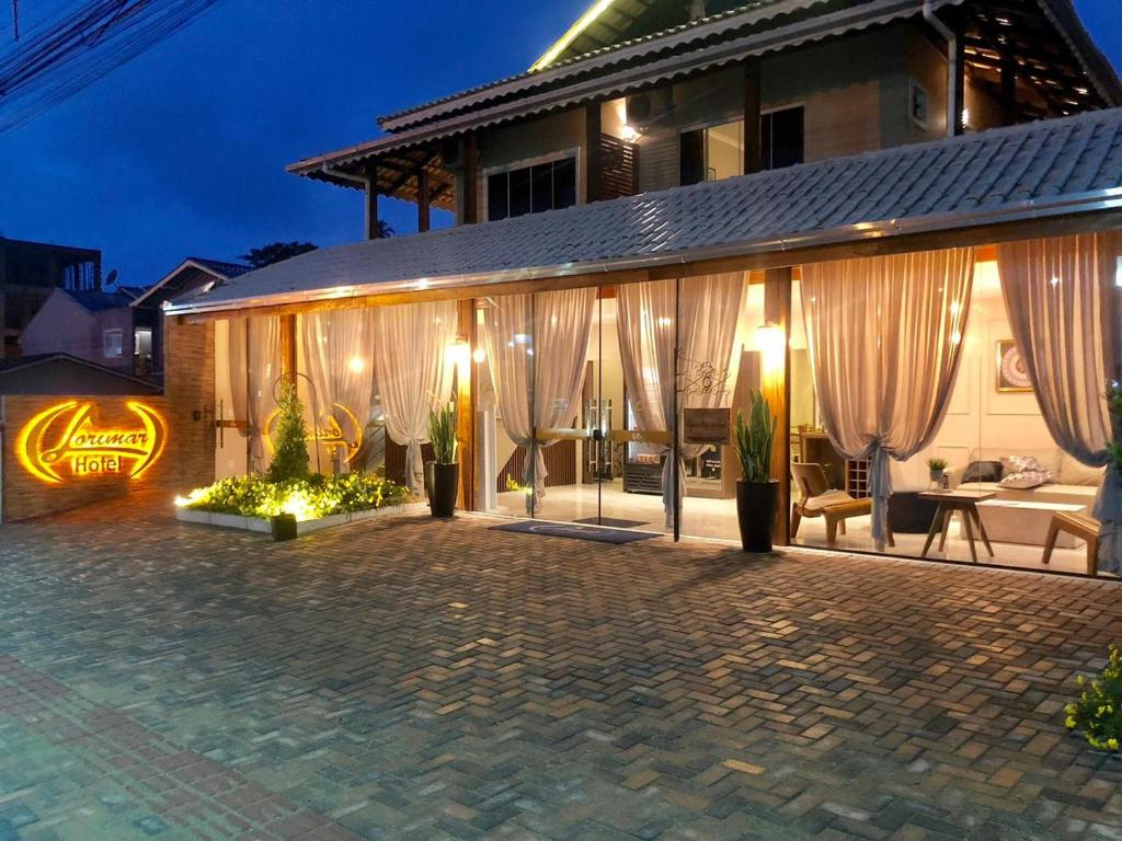 Fachada do Hotel Lorimar ao entardecer, com o letreiro iluminado e amplas vidraças