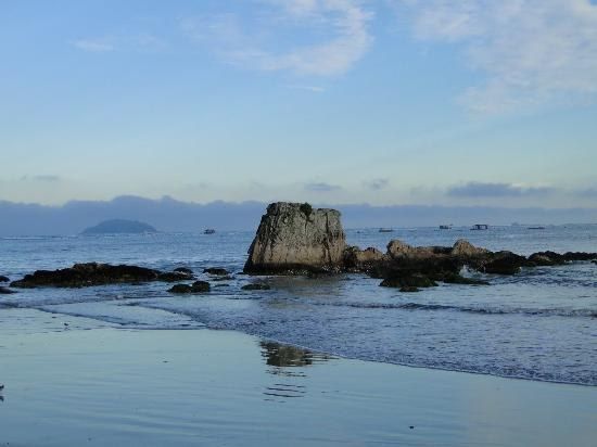 Praia da Fortaleza, em Penha, ao amanhecer, com uma grande pedra emergindo do mar calmo e ilha ao horizonte